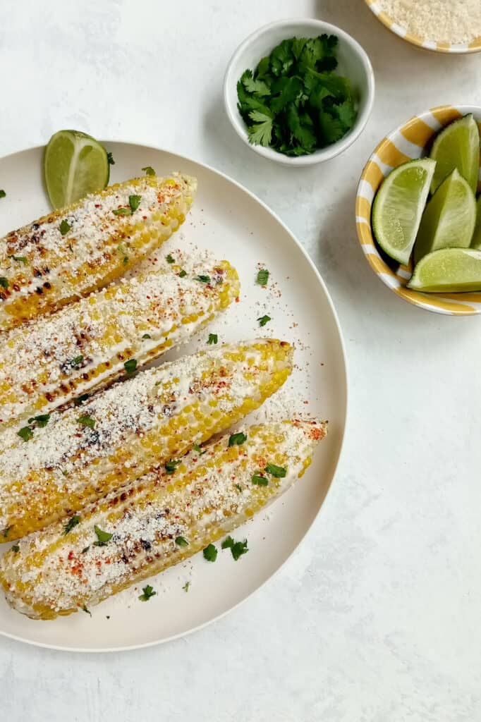 Mexican corn on the cob with a bowl of limes and Cotija cheese.