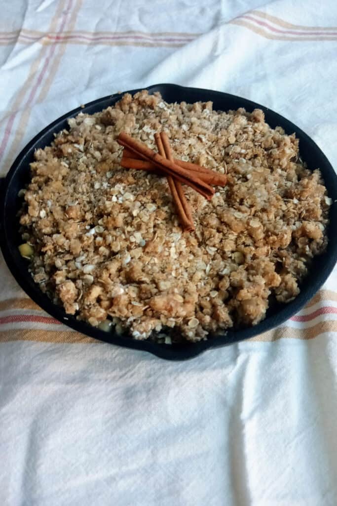 Apple crisp with oats in a skillet pan topped with cinnamon sticks.