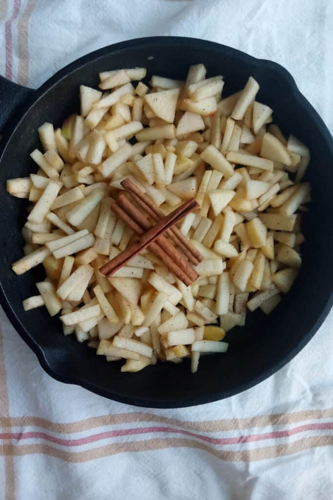 Seasoned diced apples in a skillet topped with three cinnamon sticks.