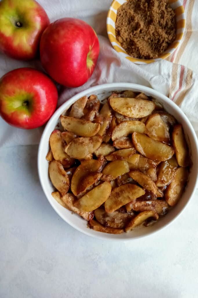 Brown sugar apples next to a small bowl of brown sugar and three honey crisp apples. 