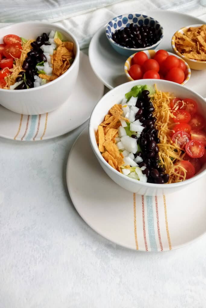 Taco salad topped with tortilla strips, black beans, white onion, grape tomatoes, and shredded cheese.