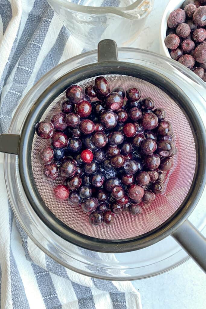 Frozen blueberries in a colander being rinsed in cold water.