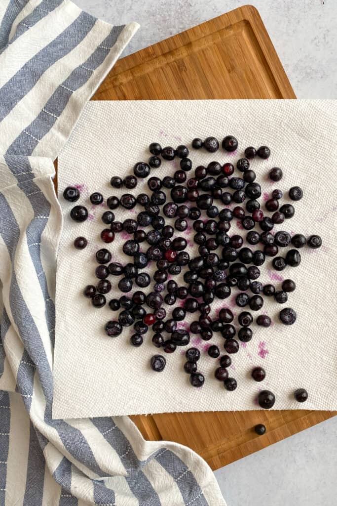 Rinsed and thawed blueberries being patted dry on a paper towel.