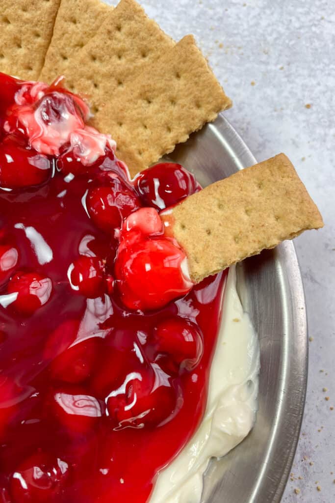 A graham cracker with cheesecake dip and a cherry on it.