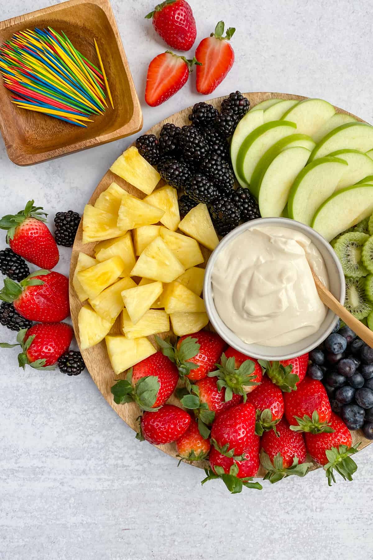 Bowl of cream cheese yogurt fruit dip on a platter with sliced fruit for dipping.