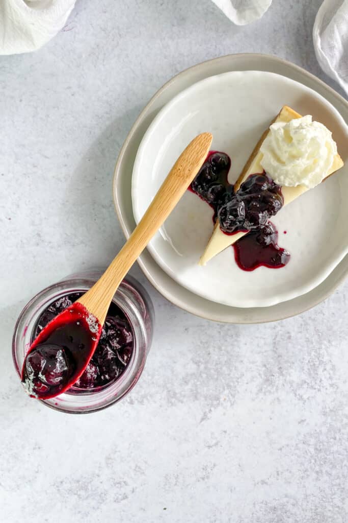 Homemade blueberry compote made with frozen blueberries served on a slice of cheesecake.