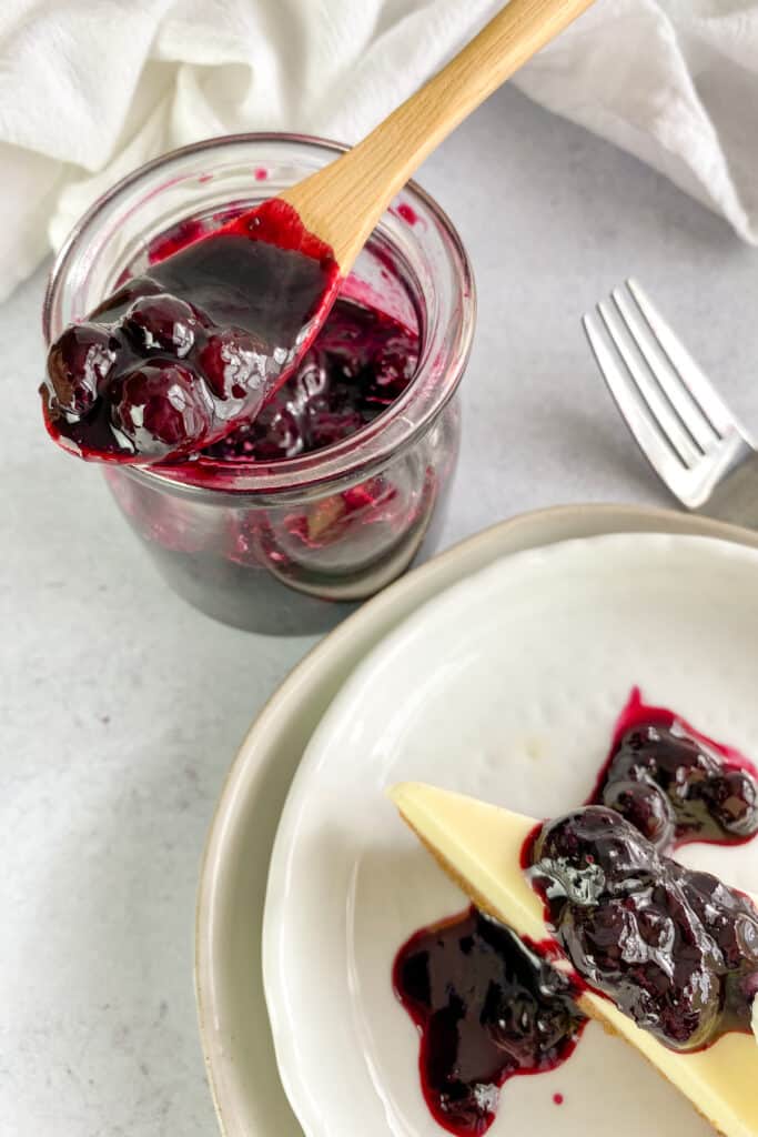 A jar of homemade blueberry compote with a spoonful or compote.