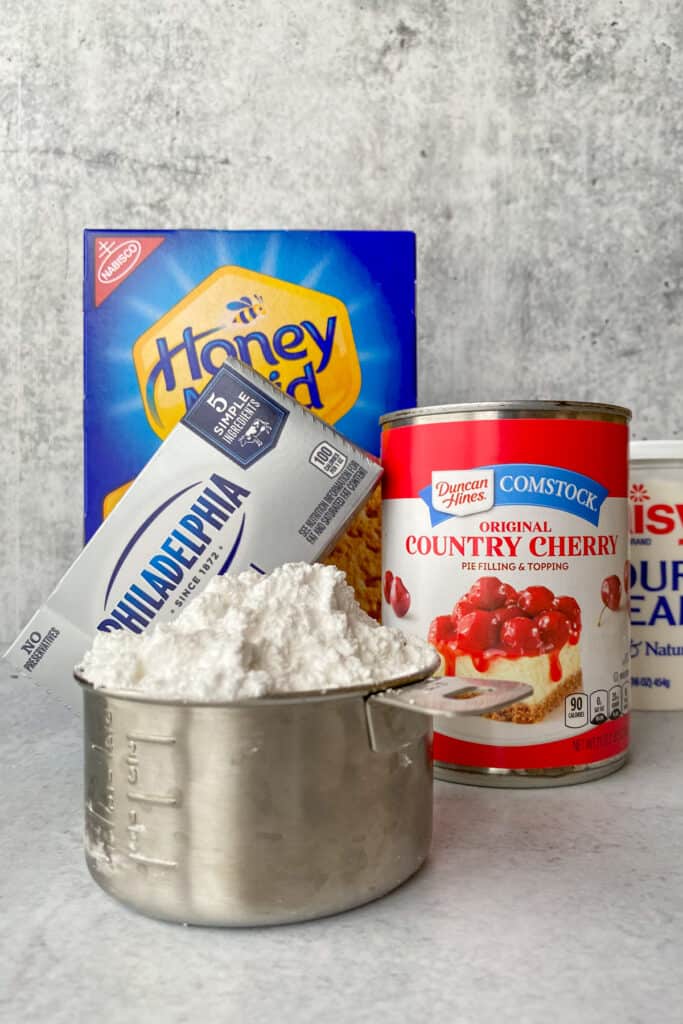 Ingredients to make cherry cheesecake dip including cream cheese, can of cherry pie filling, sour cream and powdered sugar.