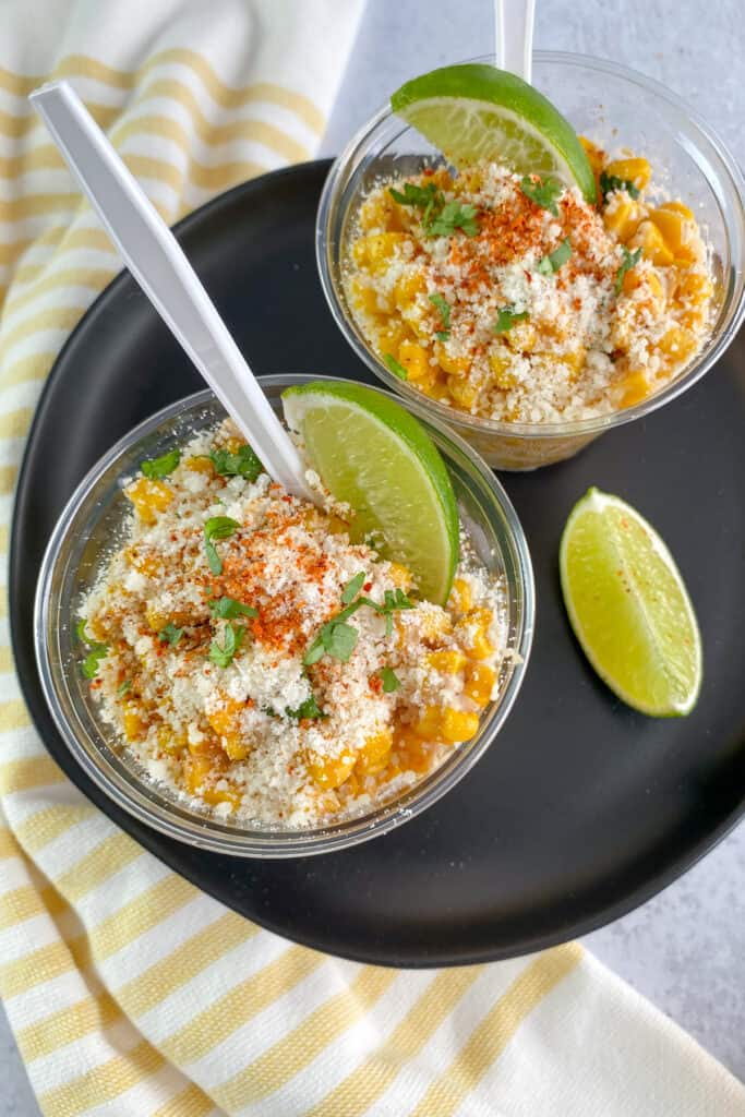Two cups of elote Mexican street corn garnished with cotija cheese, cilantro and lime.