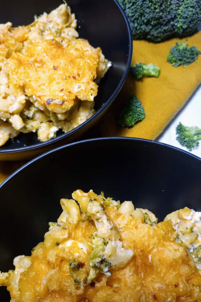 Broccoli mac and cheese in two black bowls next to a head of fresh broccoli.