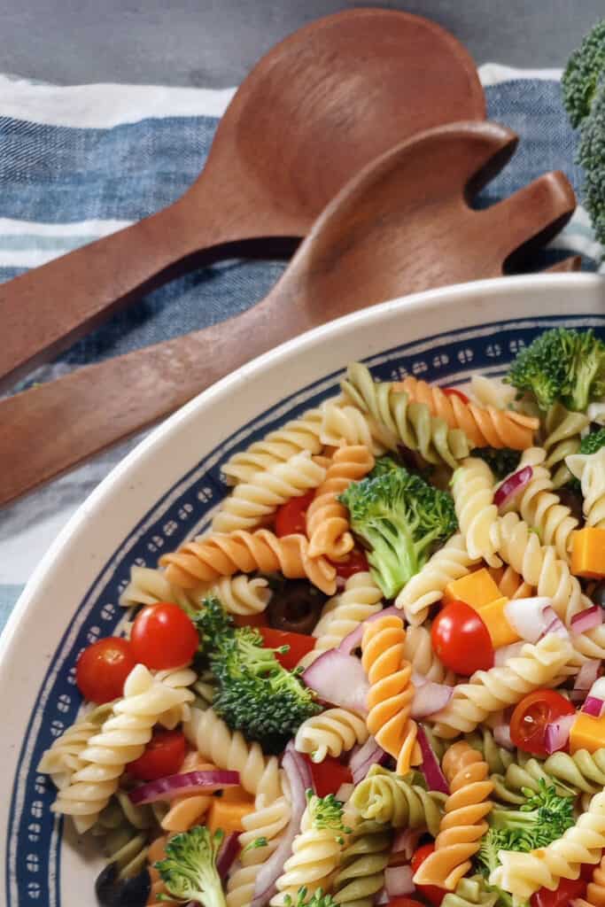 Cheddar broccoli pasta salad tossed in a salad bowl with dark wooden serving spoons. Ready to serve.
