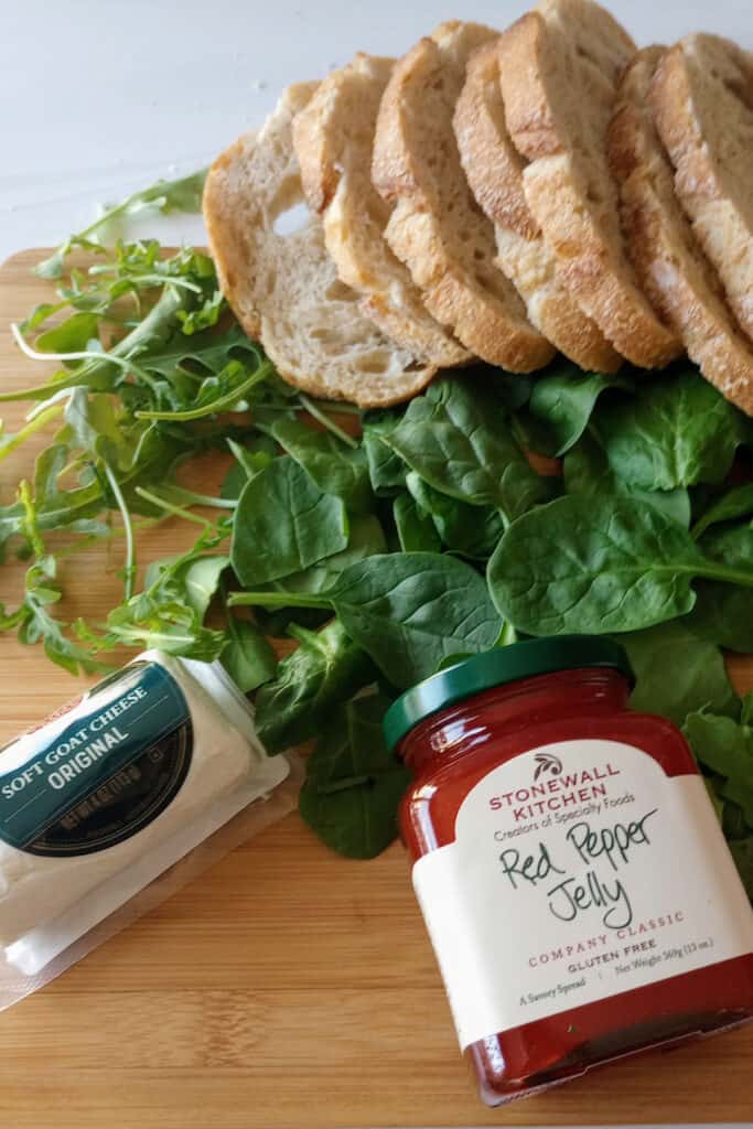 Spinach, arugula, and red pepper jelly with bread ready to be made into a sandwich. 