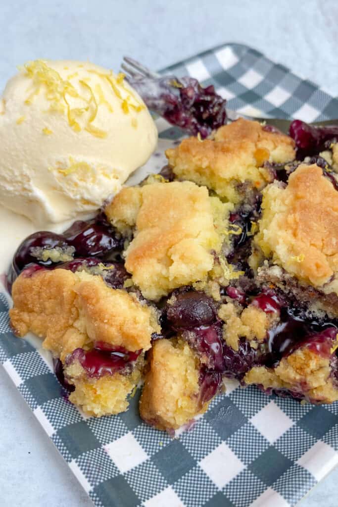 Big slice of blueberry cobbler with cake mix topping on a blue checkered plate.