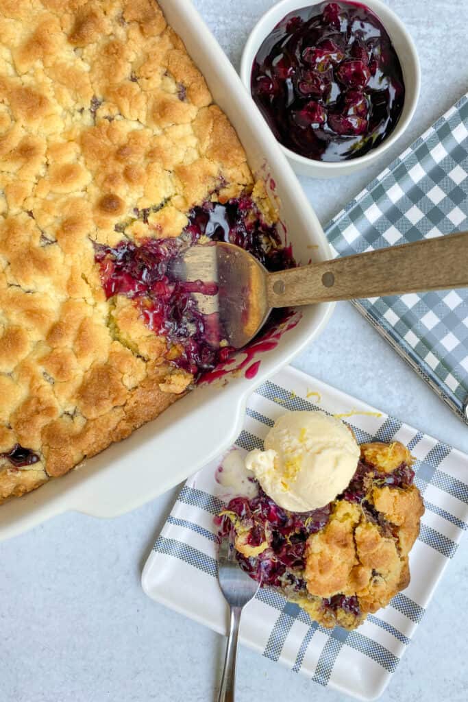 Baking dish with blueberry cobbler and spatula pulling out a serving of cobbler.