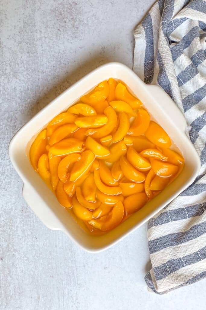 Canned peaches spread in a baking dish to make peach cobbler.