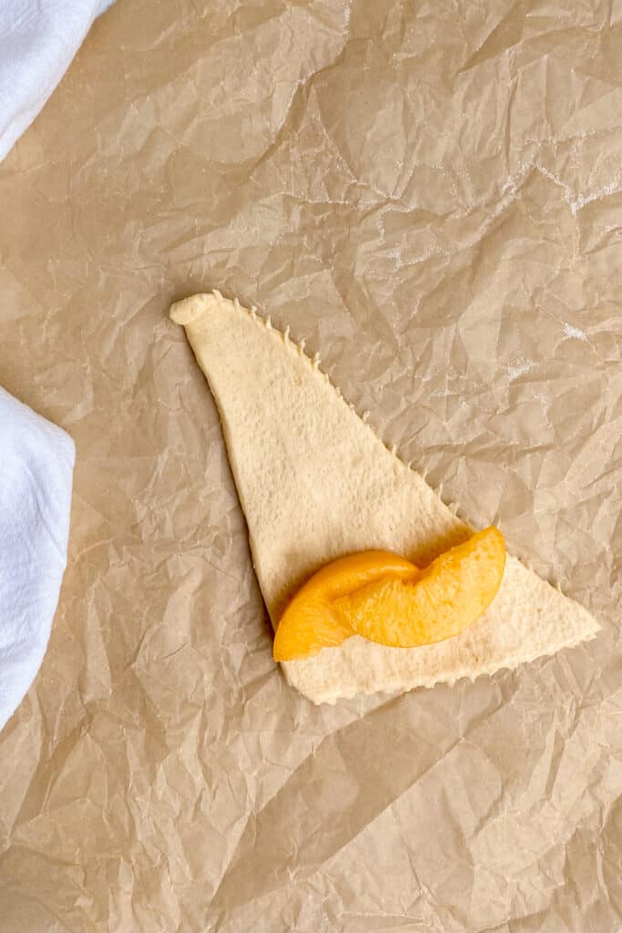 Crescent roll with two peach wedges placed on wide end before rolling.