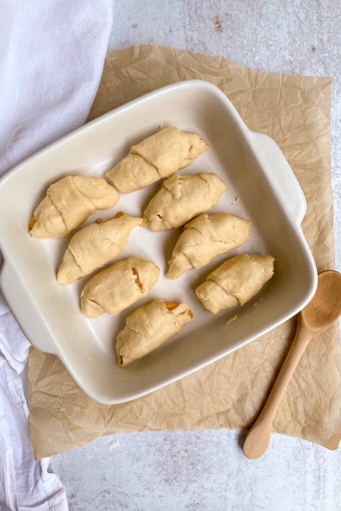 Eight peach dumplings in crescent rolls in a baking dish.