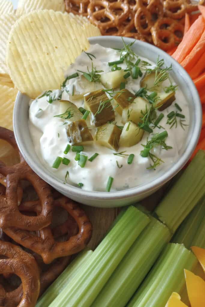 Potato chip in a bowl of dill pickle dip garnished with chopped pickles.