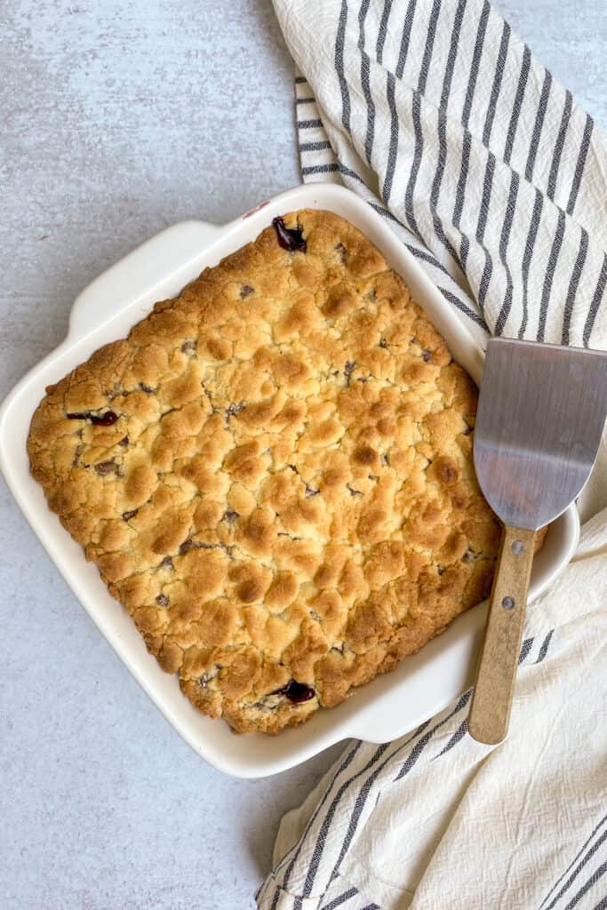 Dump cake blueberry cobbler in baking dish just out of the oven with a small spatula resting on one corner of the dish.