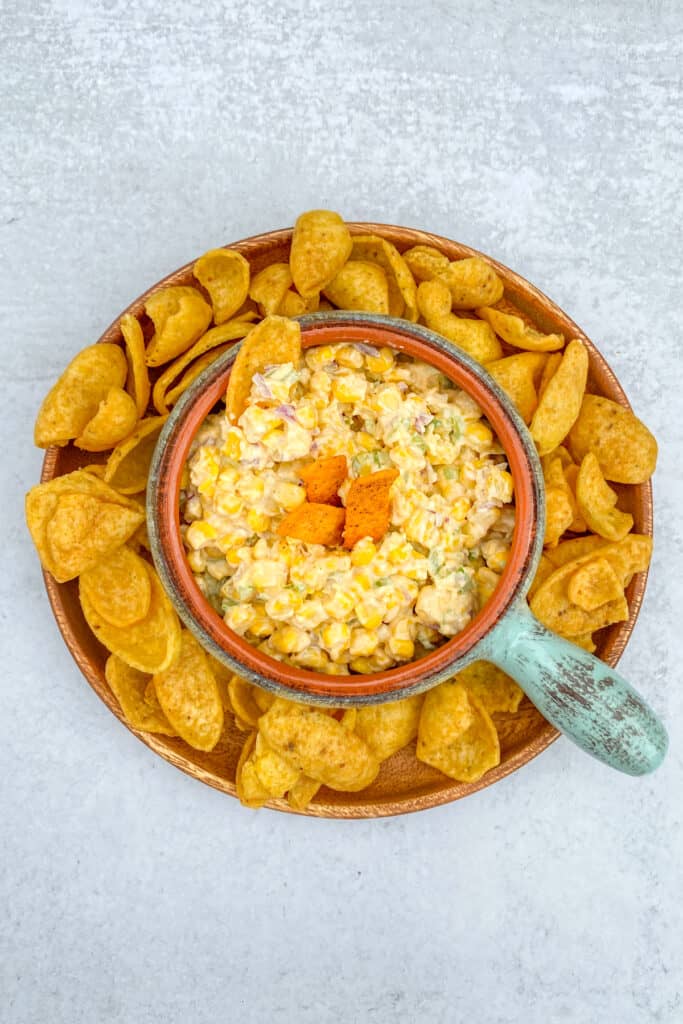 A bowl of cold Frito Corn Dip on a tray with lots of Frito chips.