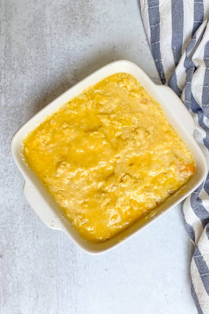 Melted butter on top of cake mix and canned peaches to make peach cobbler.