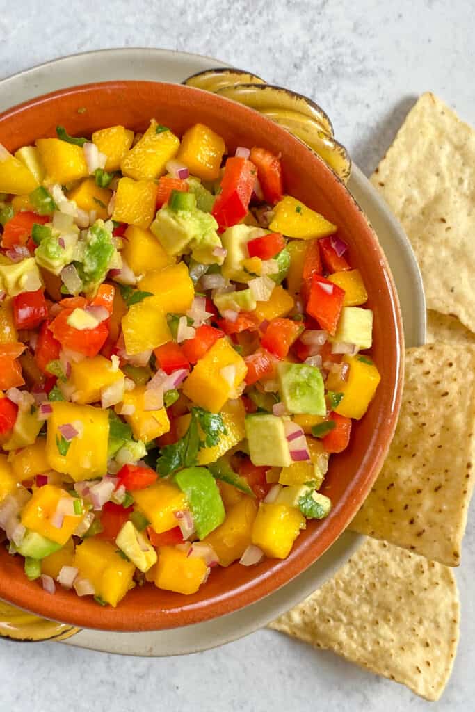 A bowl of fresh mango salsa with diced pieces of creamy avocado with tortilla corn chips on the side.