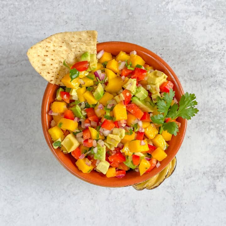 Bowl of mango avocado salsa with tortilla chip in it.