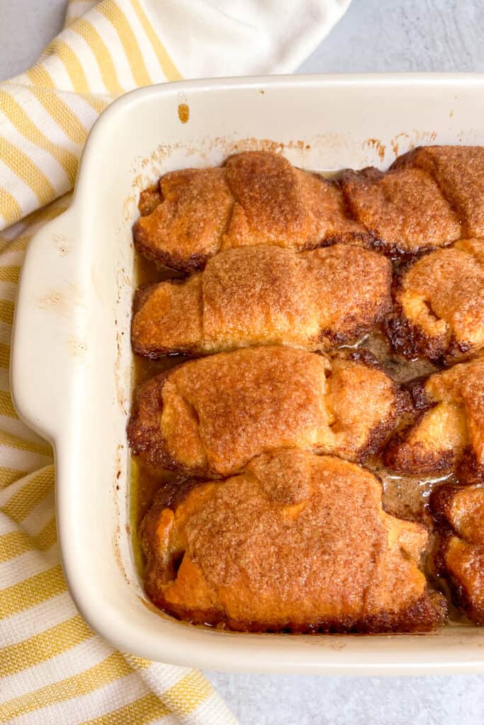 Close up of four crescent roll peach dumplings just out of the oven in the baking dish.