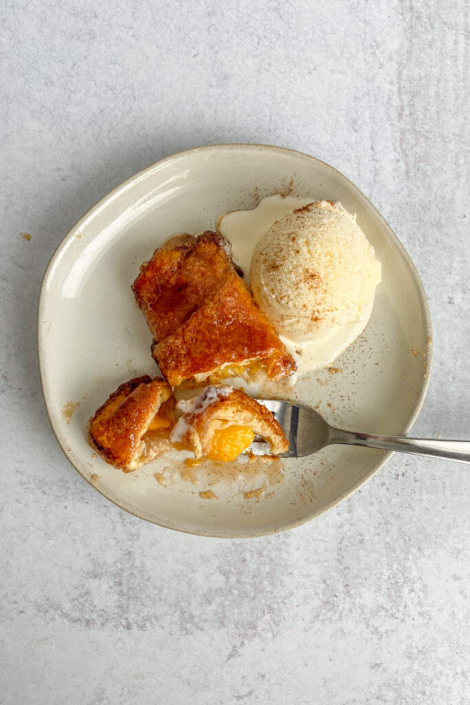 Crescent roll peach dumpling on a dessert plate with scoop of vanilla ice cream.