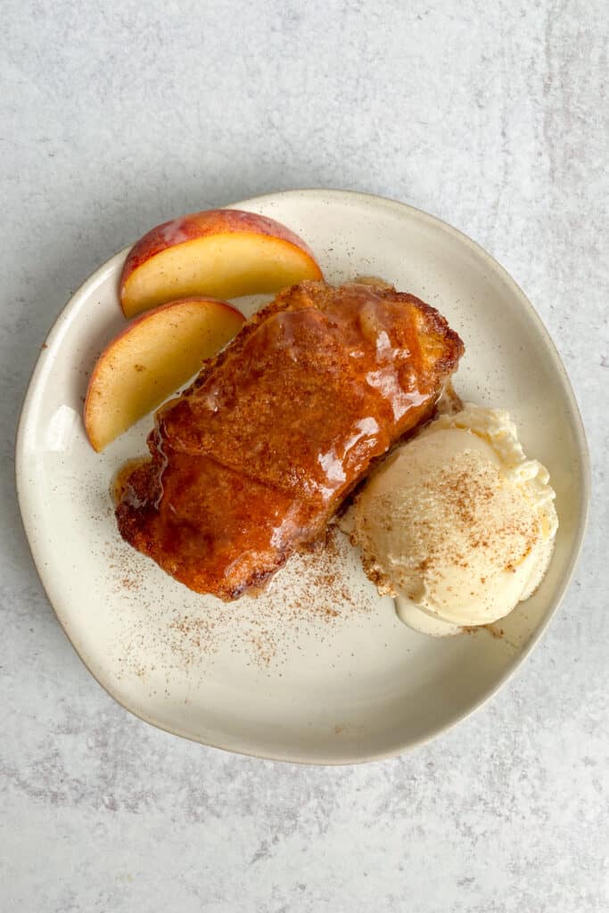 Homemade peach dumpling wrapped in a crescent roll, served with iced cream and garnished with fresh peach slices.