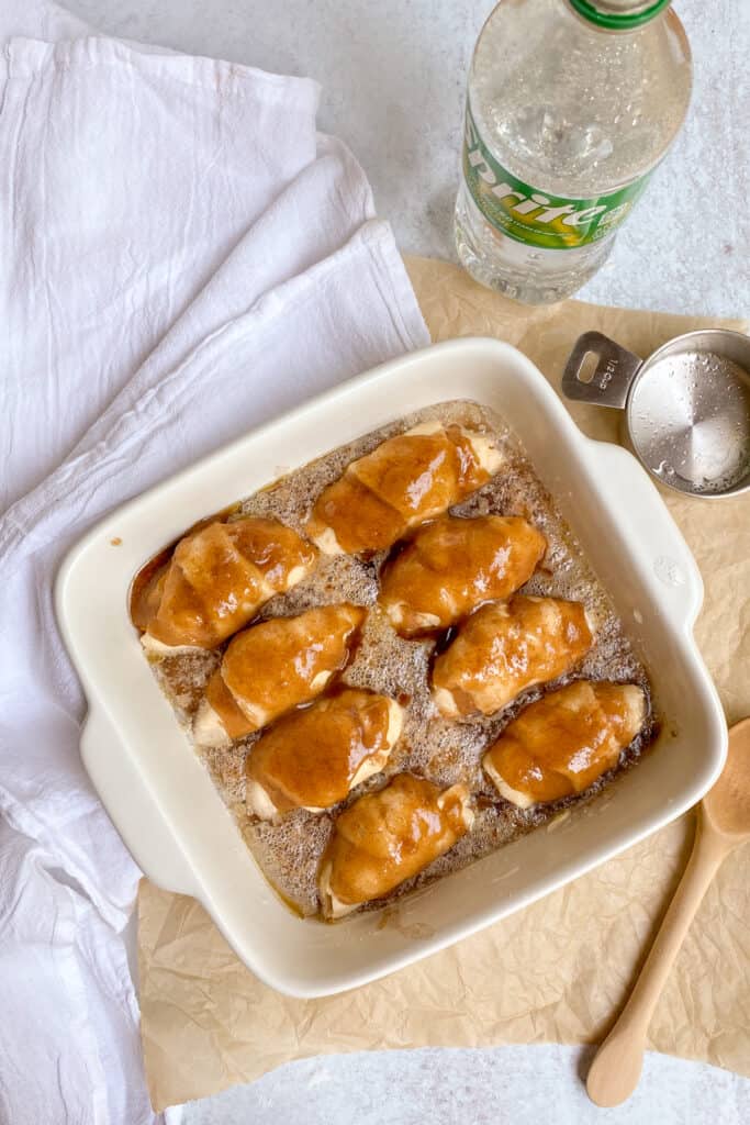 A bottle of Sprite and Sprite poured in bottom of baking dish between each peach dumpling.