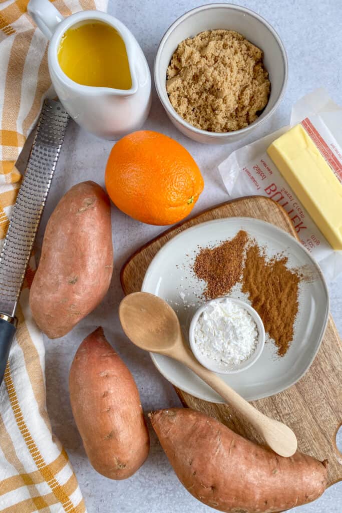 Ingredients to make candied sweet potatoes with orange juice, including whole sweet potatoes, orange juice, brown sugar, butter and orange juice.