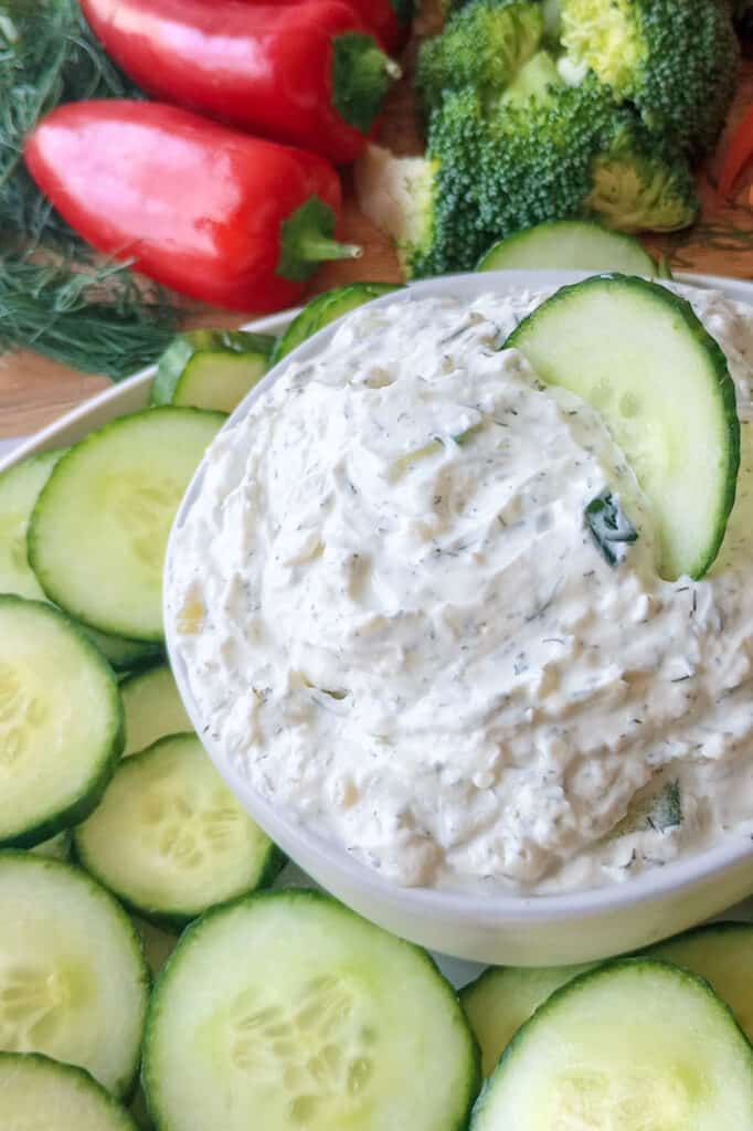 Cucumber dip garnished with thinly sliced cucumber arranged around mini red peppers, chopped broccoli heads, sliced radish, and carrot sticks. 