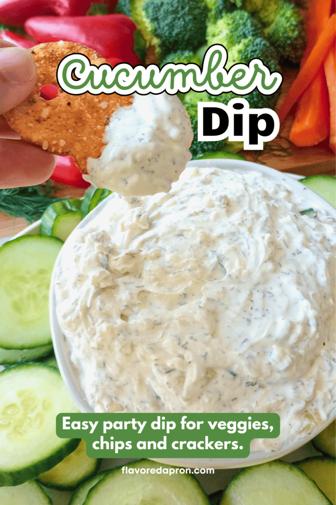 A pretzel chip being dipped into a bowl of creamy cucumber dip that's in the center of a tray full of fresh vegetables.