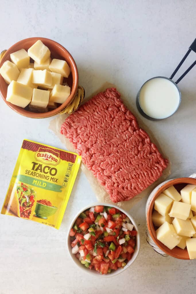 Taco seasoning, milk, homemade pico de gallo, ground meat, and cubed Velveeta cheese in measured out food bowls. 