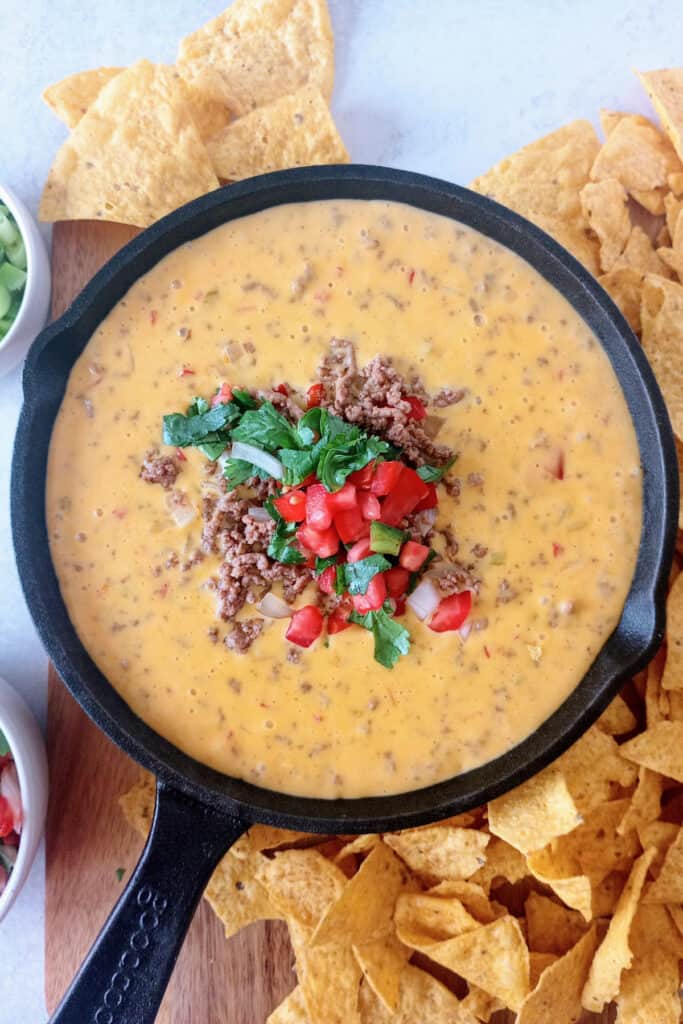 Velveeta queso dip with ground meat in a black skillet. Topped with homemade pico de gallo and served with tortilla chips.