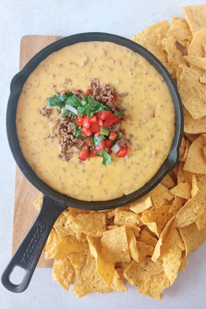 Beef queso dip in a black skillet next to tortilla chips.
