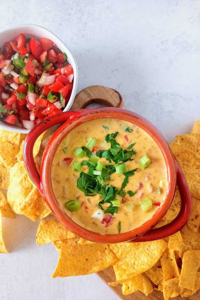 Beef queso dip in a red bowl next to homemade pico de gallo.