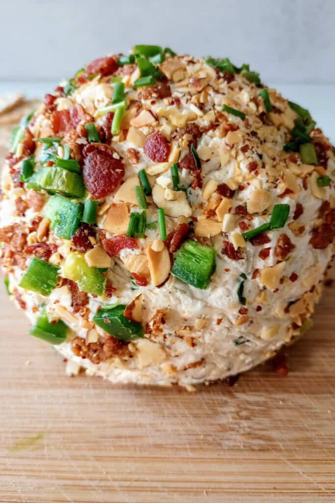 Up close of the cheese ball rolled in almonds, chives, bacon bits, diced jalapenos, and shredded cheddar cheese.