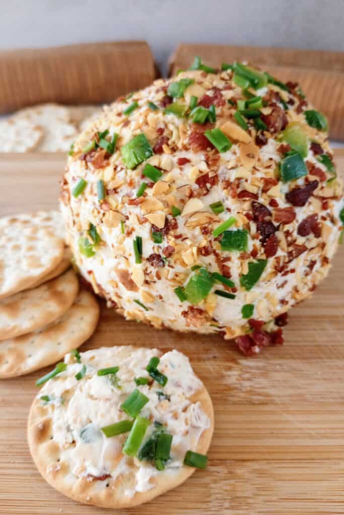 Spicy cheese ball on a brown cutting board next to crackers. 