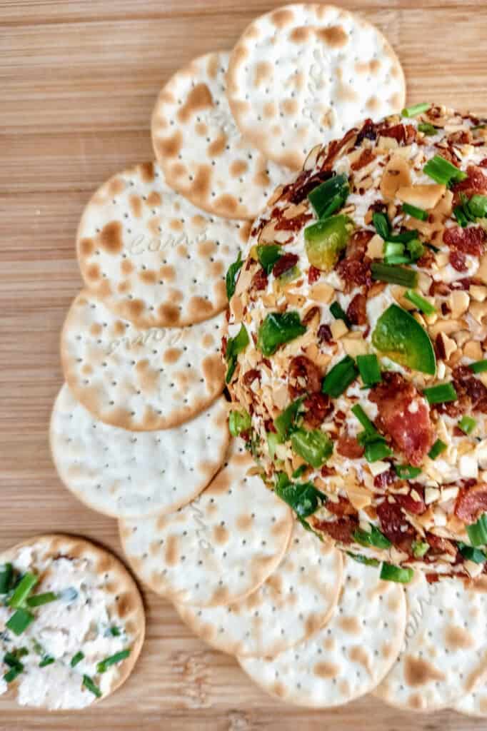 Angled cheese ball arranged around crackers. Cheese ball is rolled in almonds, cheddar cheese, and bacon bits. 