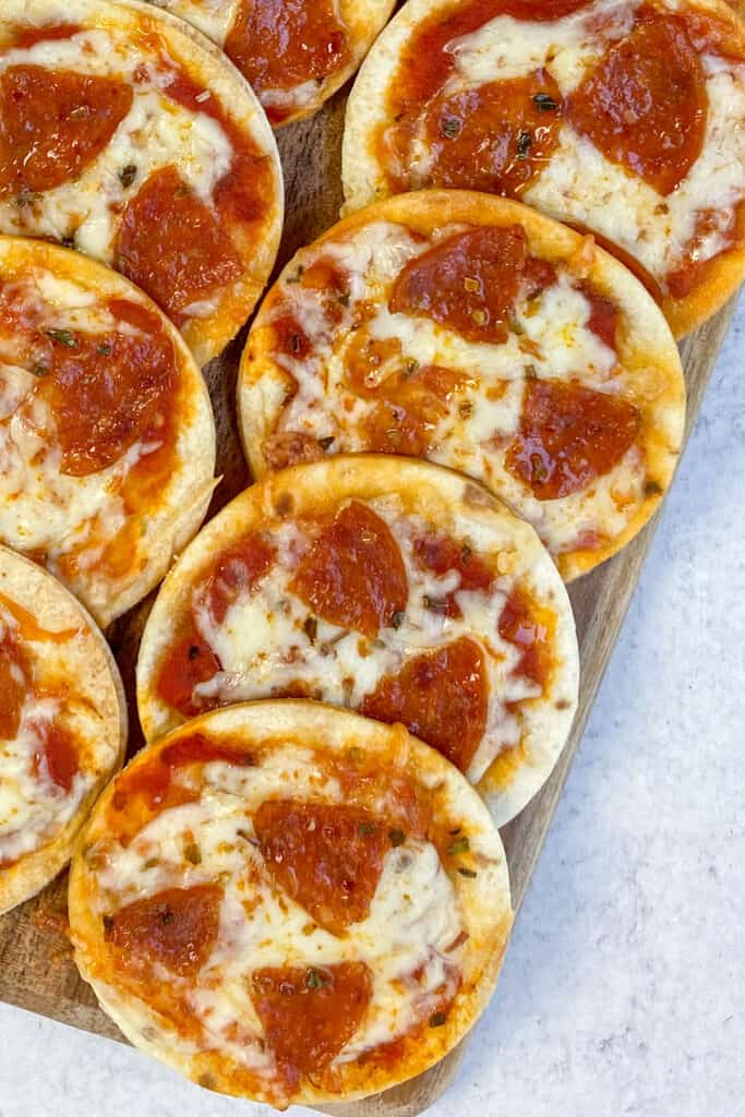 Mini tortilla pizzas with melted cheese and small pepperoni slices, lined up on a serving tray.