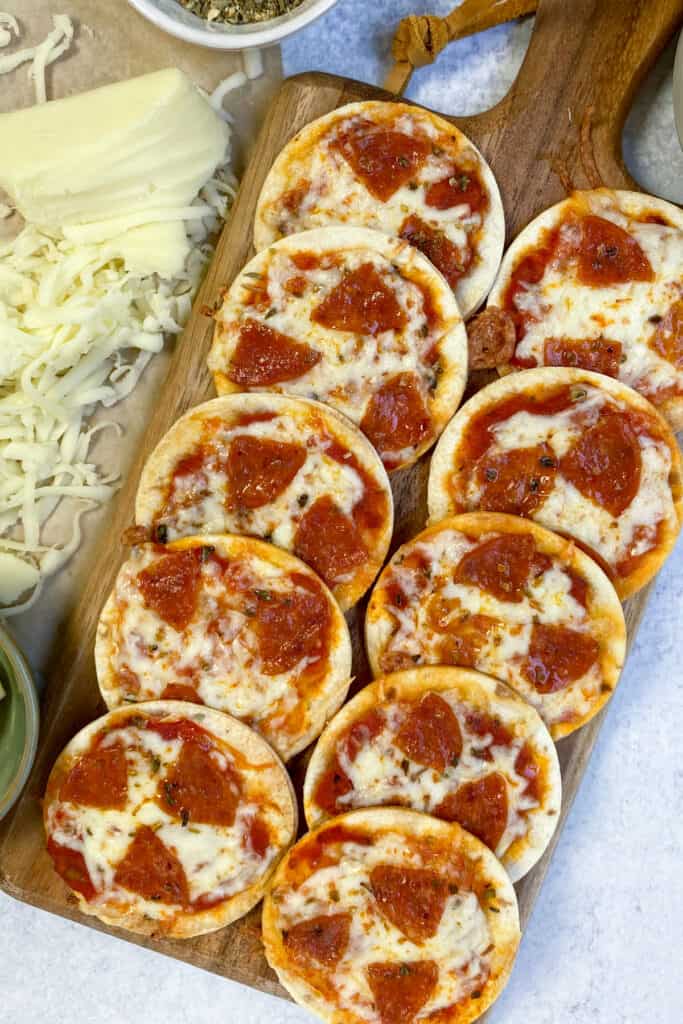 Ten small pepperoni pizzas made on flour tortillas, on a wooden board ready to serve.