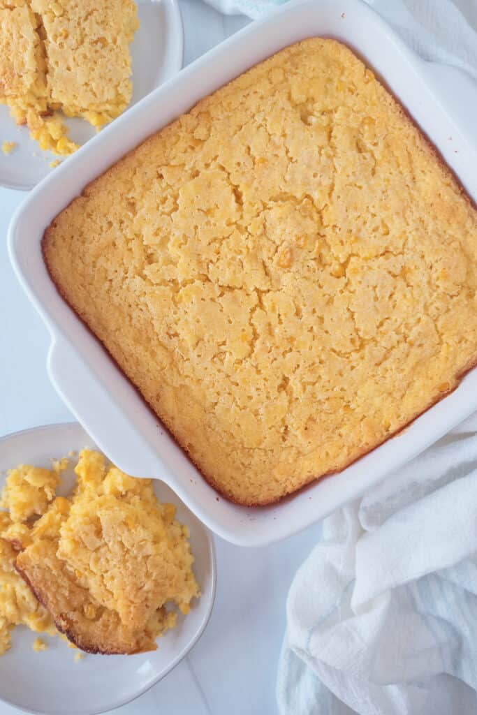 Jiffy corn casserole on a white plate next to a white casserole dish.