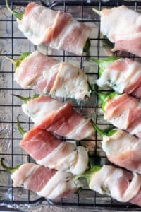 Jalapeno poppers wrapped in bacon arranged on a wire wrack ready to be cooked. 