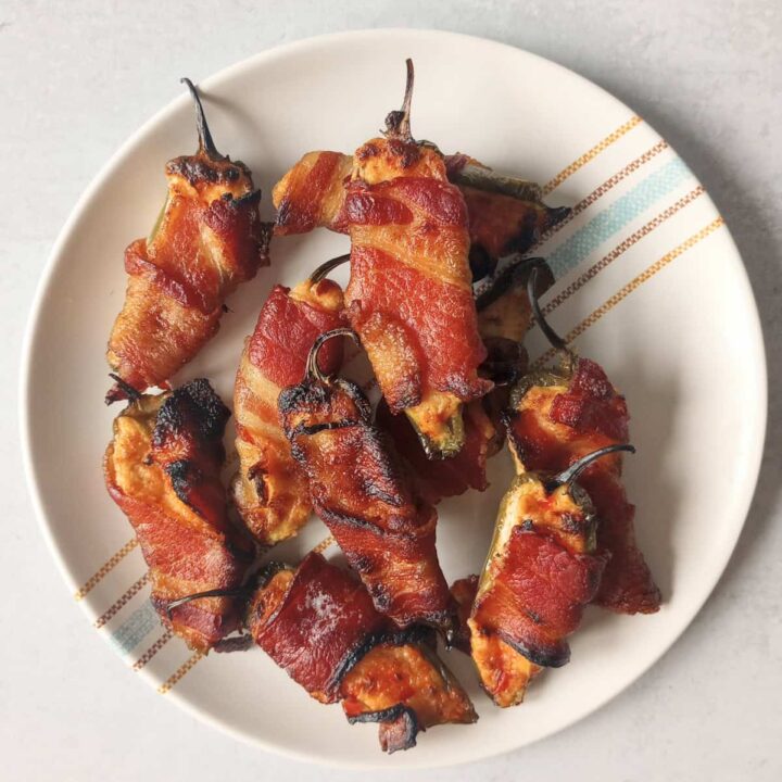 Oven baked jalapeno poppers wrapped in crispy bacon. Arranged on a white plate ready to eat.