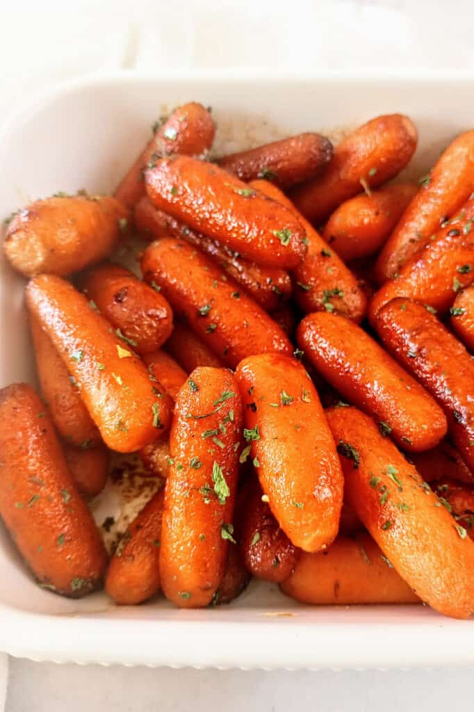 Caramelized carrots in a white baking dish garnished with parsley. 