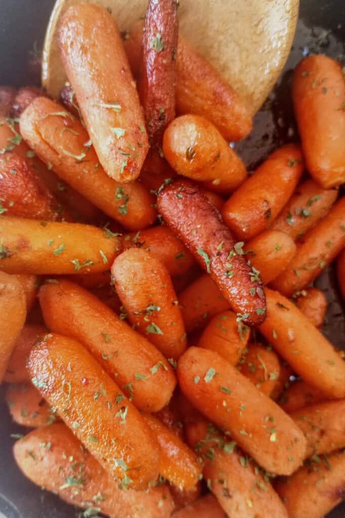 Glazed carrots in a black skillet stirred with a wooden spoon. 