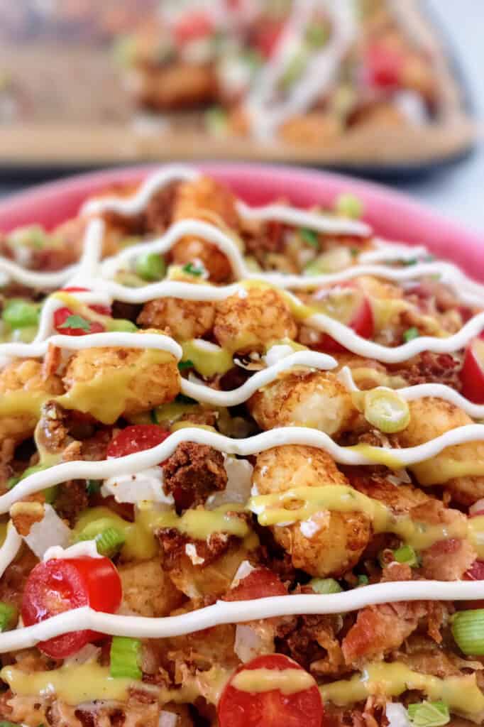 Tot-chos on a red plate next to a baking sheet. 