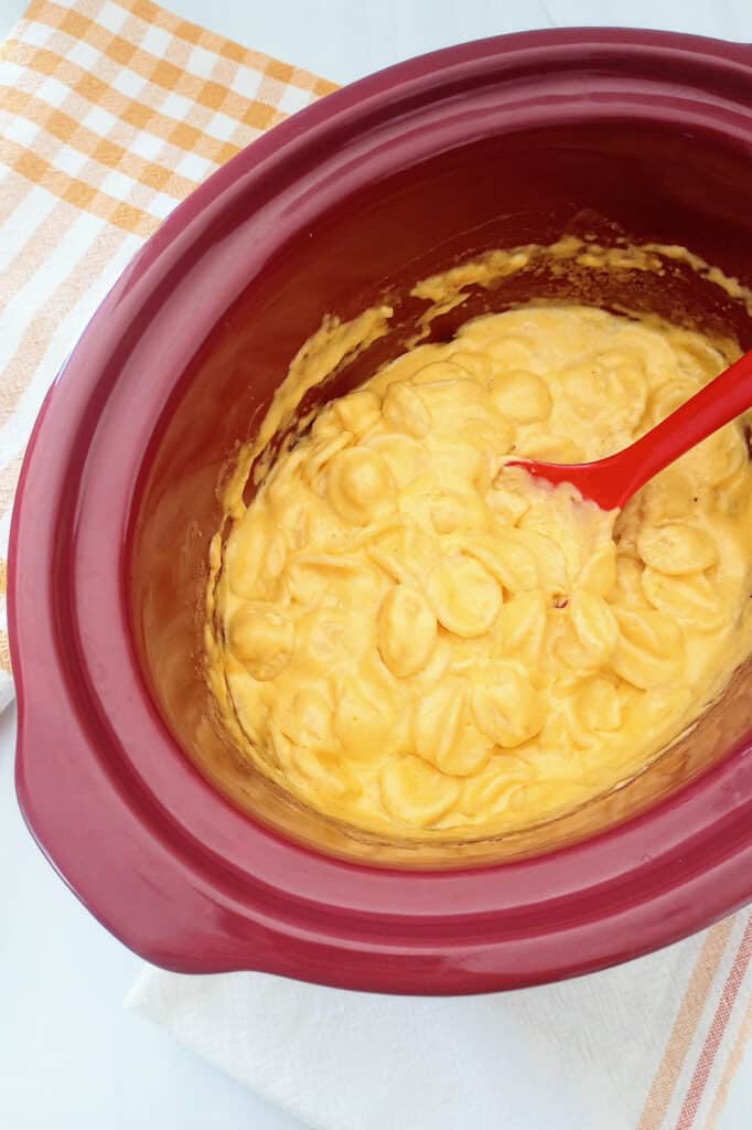 Macaroni in a red rival stoneware slow cooker next to a towel. 